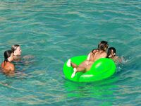 Three Nudists Laugh Together on a Bright Green Pool Float