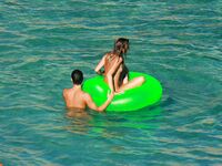 Three Nudists Laugh Together on a Bright Green Pool Float