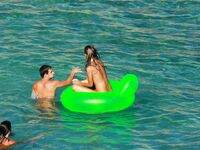 Three Nudists Laugh Together on a Bright Green Pool Float