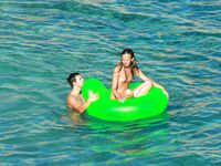 Three Nudists Laugh Together on a Bright Green Pool Float