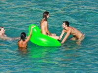 Three Nudists Laugh Together on a Bright Green Pool Float