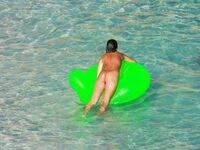 Three Nudists Laugh Together on a Bright Green Pool Float