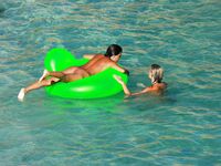 Three Nudists Laugh Together on a Bright Green Pool Float