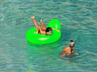 Three Nudists Laugh Together on a Bright Green Pool Float