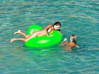 Three Nudists Laugh Together on a Bright Green Pool Float