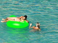Three Nudists Laugh Together on a Bright Green Pool Float