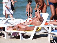 Twee topless zonnebaders kletsen op een handdoek aan een druk zandstrand
