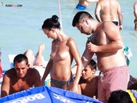 Twee topless zonnebaders kletsen op een handdoek aan een druk zandstrand