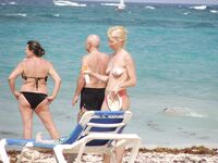 Pelle lucida al sole in slip gialli sulla riva di una spiaggia topless