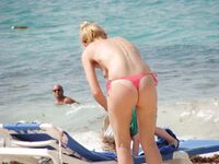 Pelle lucida al sole in slip gialli sulla riva di una spiaggia topless
