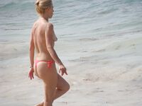 Pelle lucida al sole in slip gialli sulla riva di una spiaggia topless