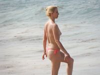 Pelle lucida al sole in slip gialli sulla riva di una spiaggia topless