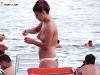 Si raccoglie i capelli scuri al mare su una tranquilla spiaggia nudista