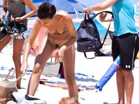 A Couple Leaves Turquoise Shallows Near a Striped Umbrella on a Nude Beach