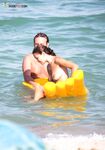 A Camera Bag on Wet Sand as Two Nudists Pause at the Water's Edge