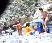Sonrisa con las manos tras la nuca en una playa nudista rocosa