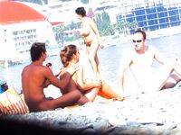 Sonrisa con las manos tras la nuca en una playa nudista rocosa