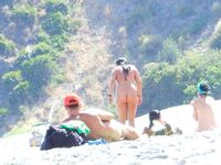 Sonrisa con las manos tras la nuca en una playa nudista rocosa
