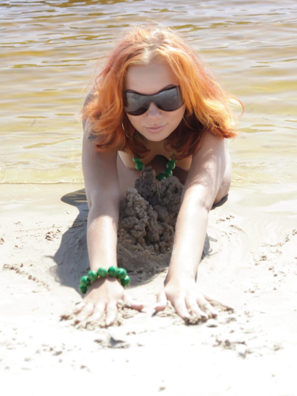 Rudowłosa topless z zielonymi koralikami bawi się w piasku album preview