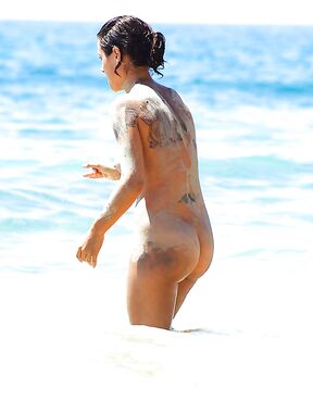 Fraîchement sortie des vagues, tatouages et sable collé à la peau sur le rivage